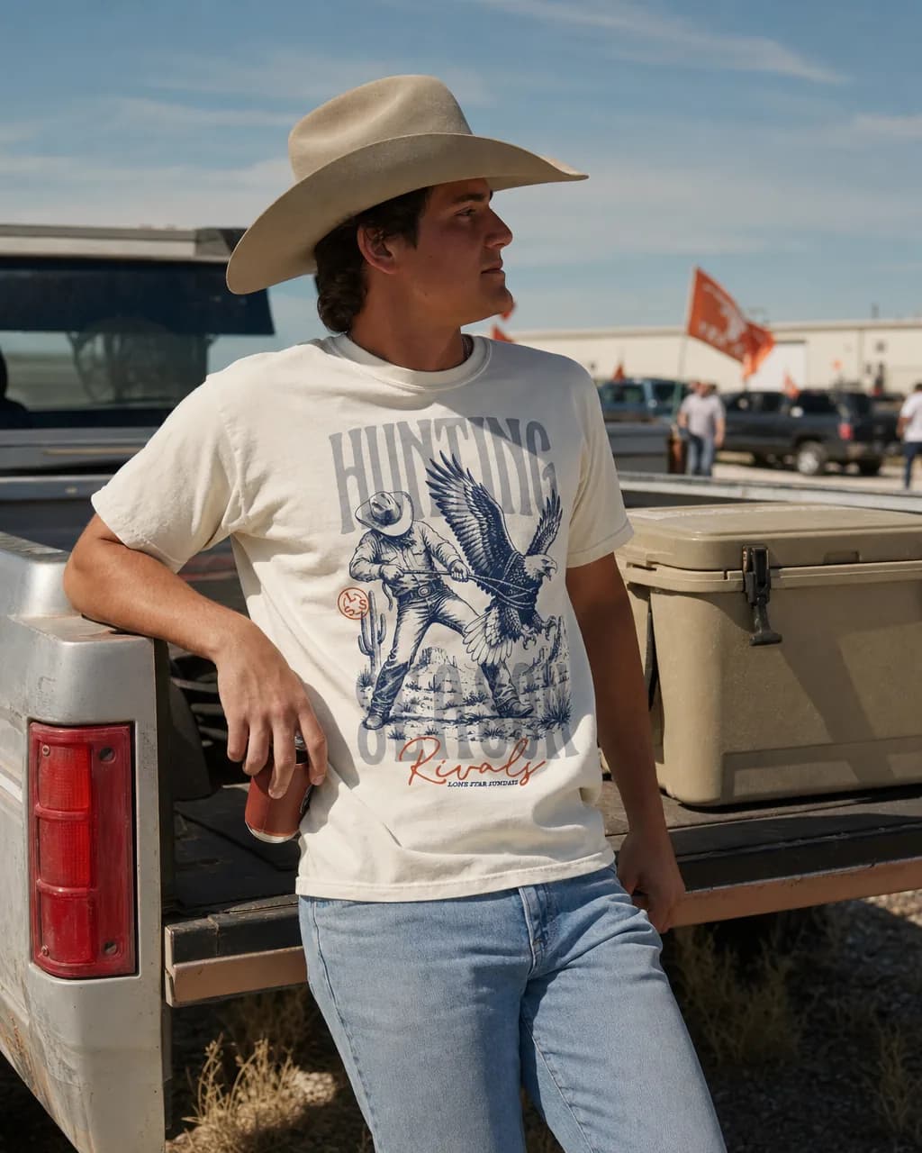 Man in a cream vintage Dallas football fan tee at a truck tailgate, Hunting Season cowboy-and-eagle graphic